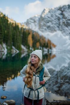 a woman with long hair standing in front of a mountain lake and looking up at the sky