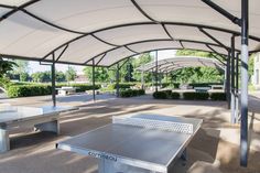 two ping pong tables in an enclosed area with trees and bushes behind them on either side of the pavilion