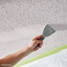 a hand holding a spatula in front of a ceiling with white paint on it