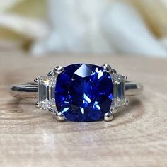 a blue ring with three baguets on the side and an oval cut diamond in the middle