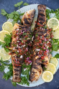 two fish on a plate with lemons and cilantro garnishes