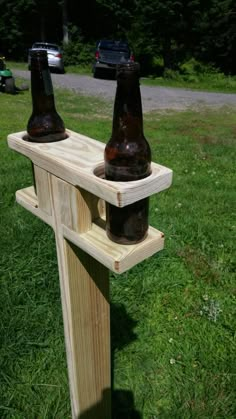 two beer bottles sitting on top of a wooden bench in the grass next to a car