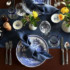 the table is set with blue and white dishes, silverware, and napkins