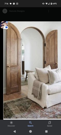 a living room with white furniture and wooden doors on the wall, in front of an arched doorway