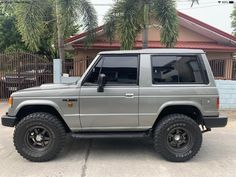 a silver suv parked in front of a house with palm trees behind it and a gate