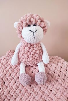 a crocheted stuffed animal sitting on top of a pink blanket in the shape of a sheep