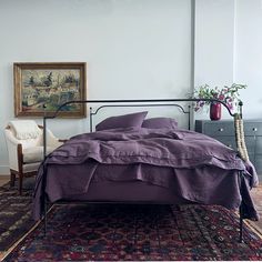 a bed sitting on top of a rug next to a chair and painting above it