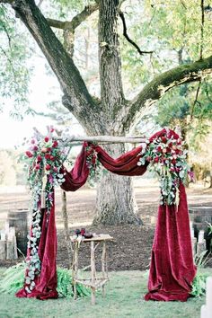 an outdoor ceremony setup with red velvet drapes and white flowers on the back drop