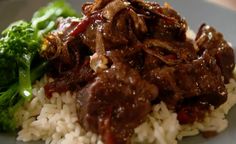 a white plate topped with beef and onions on top of rice next to a fork