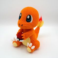 an orange crocheted stuffed animal holding a red object in it's paws