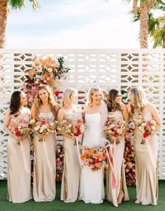 a group of women standing next to each other holding bouquets in front of a white fence