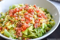 a white bowl filled with lettuce, tomatoes and other toppings on top of it