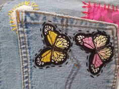 two butterflies are on the back of a pair of blue jean pants with pink and yellow accents