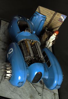 a blue car engine sitting on top of a table next to a man in a suit