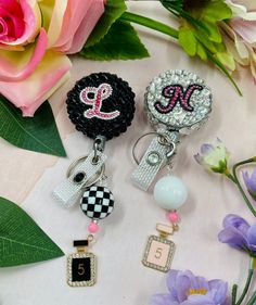 three keychains with different designs on them sitting next to some flowers and pink roses