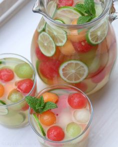 two pitchers filled with fruit and mint garnish on top of a white table