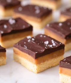 chocolate and peanut butter squares are arranged on a white surface with other desserts in the background