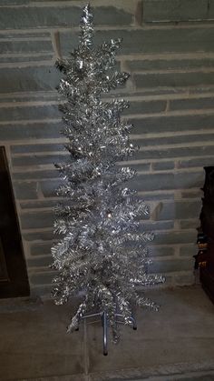 a silver tinsel christmas tree sitting in front of a brick wall on a metal stand