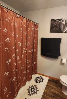 a bathroom with a toilet, shower curtain and rug on the wooden floor next to it