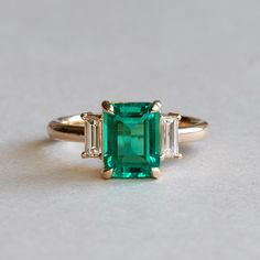 Lab grown emerald adorned with baguette diamondsCut: EmeraldThree stone ringStone Size: 8 x6 mmBaguette Diamonds: Two 4.5 x 2 mmDiamond Clarity: SIDiamond Color: GHIDiamond weight: 0.12 carat eachTotal Diamond Weight: 0.25 caratMetal Type: 18 karat gold Emeral Rings, Emerald Gold Ring Vintage, Emerald 3 Stone Ring, Three Stone Emerald Ring, Diamond Ring With Emerald Accents, Emerald Cut Emerald Engagement Ring, Emerald Stone Engagement Ring, Emerald Green Engagement Ring, Diamond And Emerald Engagement Ring