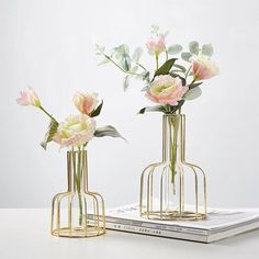 two vases with flowers in them sitting on a table next to a book and magazine