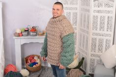 a man standing next to a pile of balls of yarn in a room with white walls