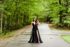 a woman in a long black dress is walking down the road with her hand on her head