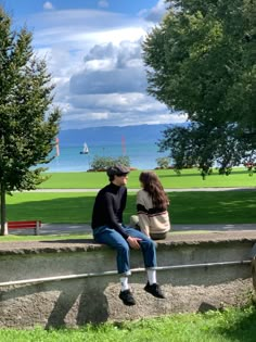 two people are sitting on a bench looking out at the water and trees in front of them