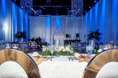 a table set up for an event with white flowers and blue drapes on the walls