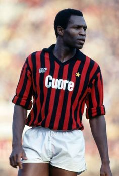 a soccer player in red and black uniform standing on the field with his hands behind his back