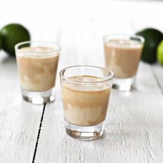 three shot glasses filled with ice cream and two limes on the table behind them