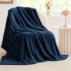 a blue knitted blanket sitting on top of a white chair next to a window