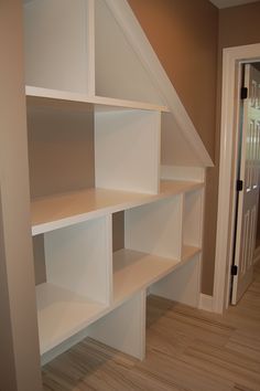 an empty room with white shelves and wood flooring in front of a door that leads to a hallway