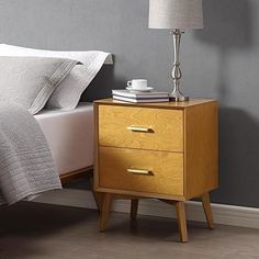 a nightstand with two drawers and a lamp next to it on top of a bed