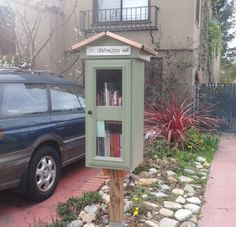 a small green book case sitting on the side of a road next to a car