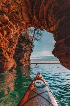 a kayak is in the water next to a large rock formation that looks like an arch