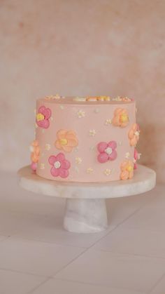 a pink cake with flowers on it sitting on top of a white pedestal in front of a wall