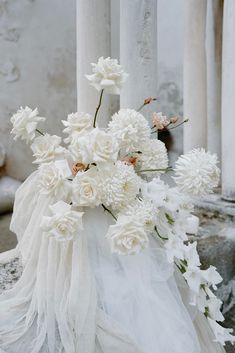 a bouquet of white flowers sitting on top of a stone bench next to pillars with columns in the background