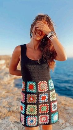 a woman standing on top of a rocky cliff next to the ocean holding her hair