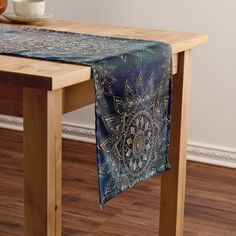 a blue table runner with an intricate design on it, sitting on a wooden table