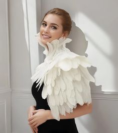 a woman in black dress with white wings on her neck and shoulders, posing for the camera