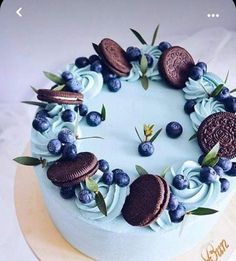 a cake decorated with blue frosting, cookies and berries is on top of a plate