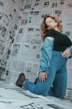 a woman laying on top of a bed next to a wall covered in newspaper sheets