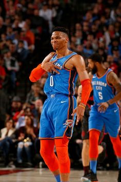 two basketball players in blue and orange uniforms are standing on the court with their hands together