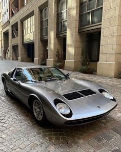 a silver sports car parked in front of a brick building on a cobblestone street