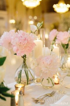 there are many flowers in vases on the table with candles and lights behind them