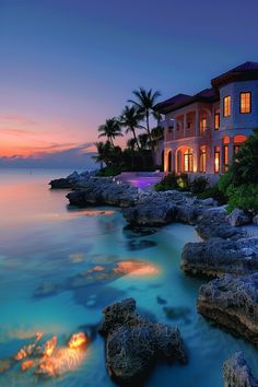 a large house sitting on top of a lush green hillside next to the ocean at sunset