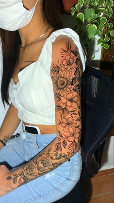 a woman wearing a face mask and sitting on a chair with flowers tattooed on her arm