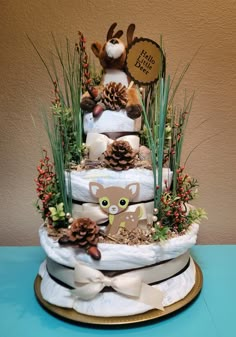 a three tiered cake decorated with pine cones and fake animals is on a blue table