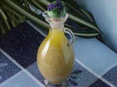 a glass bottle filled with yellow liquid sitting on top of a blue table cloth next to green plants